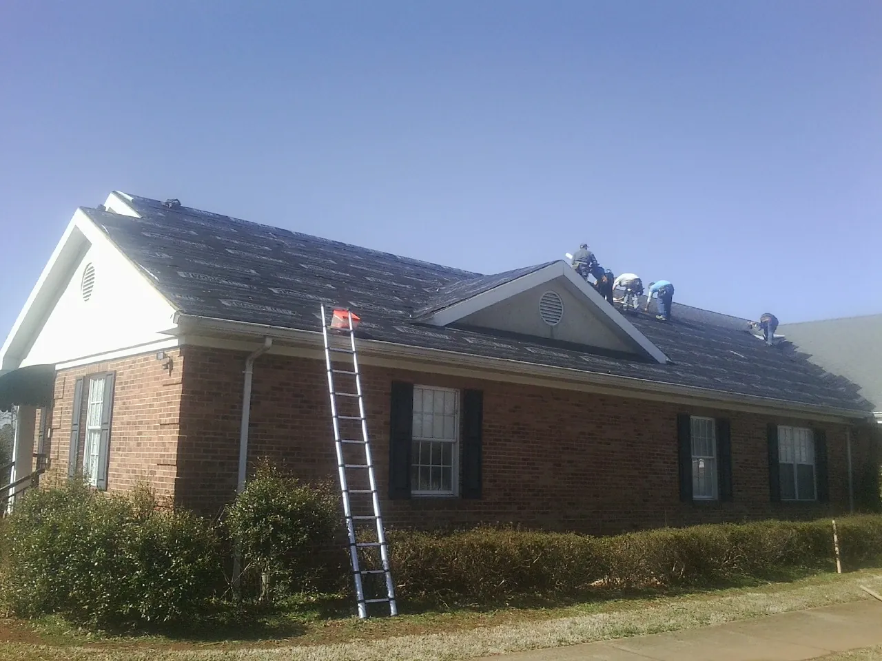 Crew tearing shingles off a brick ranch roof with a ladder set — Emergency Roof Repair work by our crew in Theodore