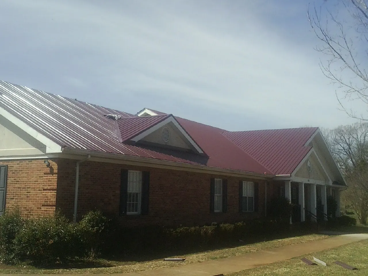 Red metal roof with gabled entries on a long brick building, from a Hail Damage Roof Repair job in Theodore