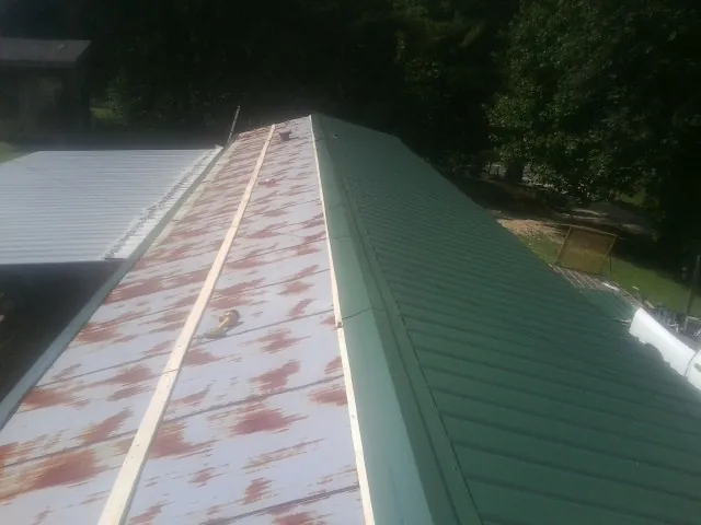 Old rusted panels beside newly installed green metal roofing — Wind Damage Roof Repair by Roofing Brothers in Theodore
