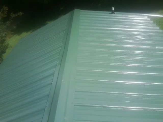 New green metal panels meeting at the ridge of a roof — Flat Roof Repair work by our crew in Theodore