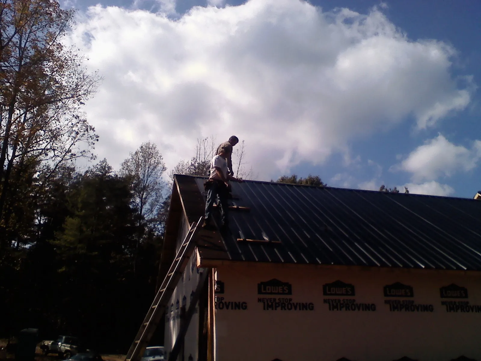 Roofer fastening dark metal panels high against a cloudy sky, from a Roof Inspection job in Theodore