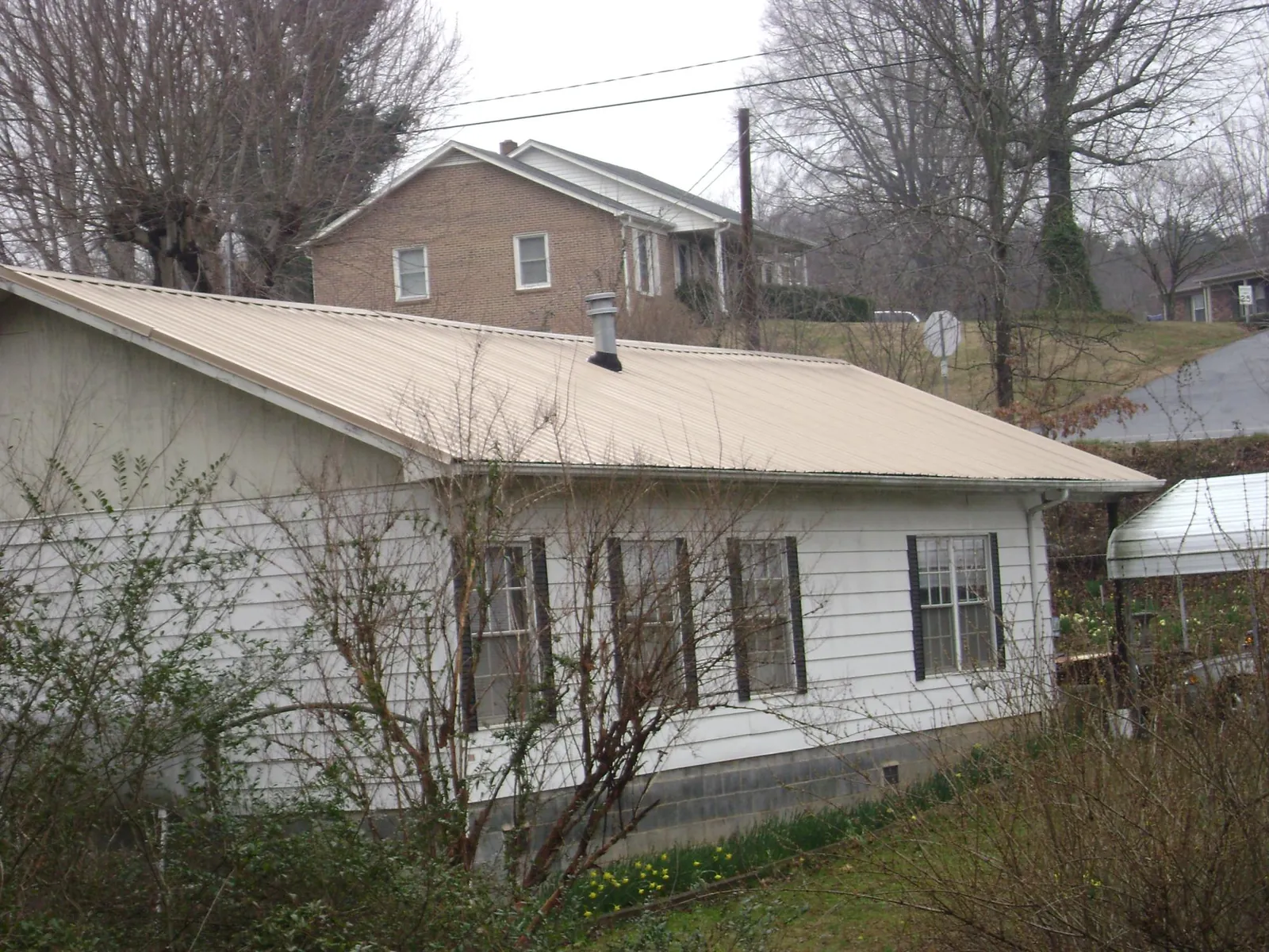 Tan metal roof on a white sided house set into a hillside — Commercial Roofing by Roofing Brothers in Theodore