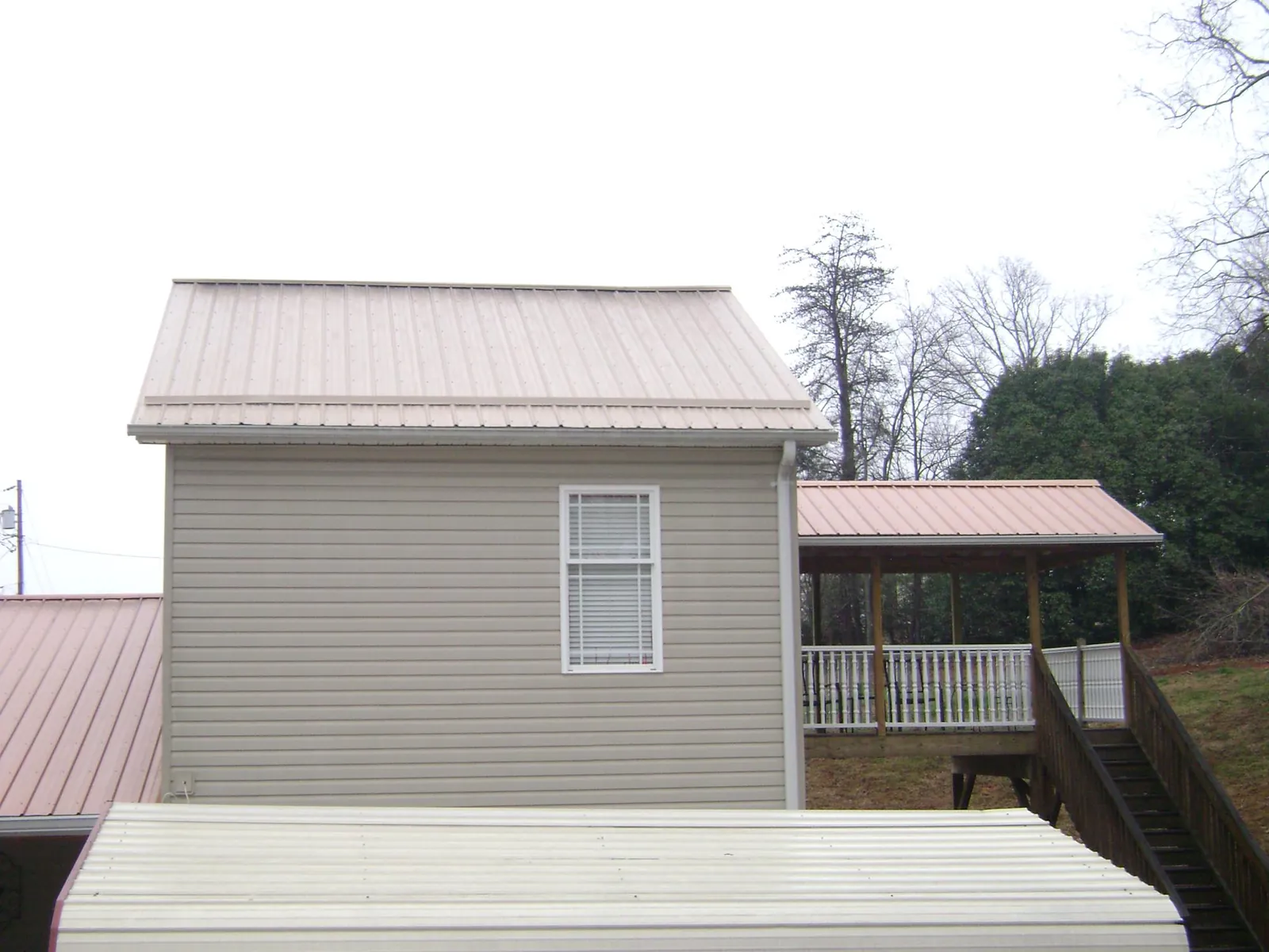 Tan metal roofs on a two story addition and attached porch, from a Roof Replacement job in Theodore