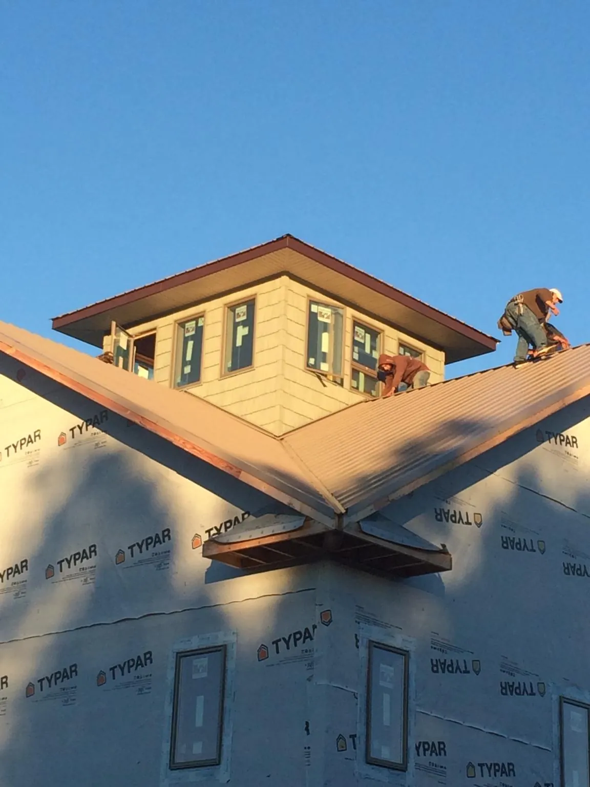 Roofers working around a rooftop cupola on a new metal roof at sunset — Roof Waterproofing in Theodore by Roofing Brothers